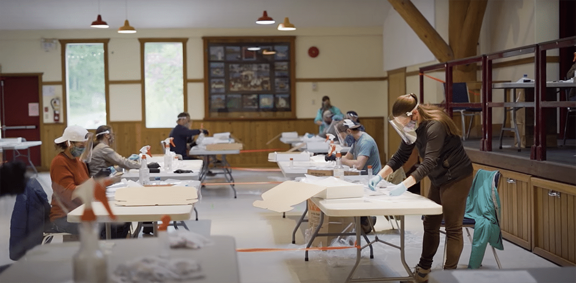 People wearing masks and working at tables in a spacious room with wooden decor.