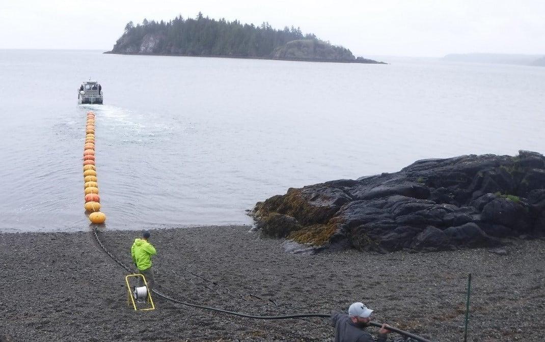 Boat towing yellow buoys across a rocky shore toward an island.