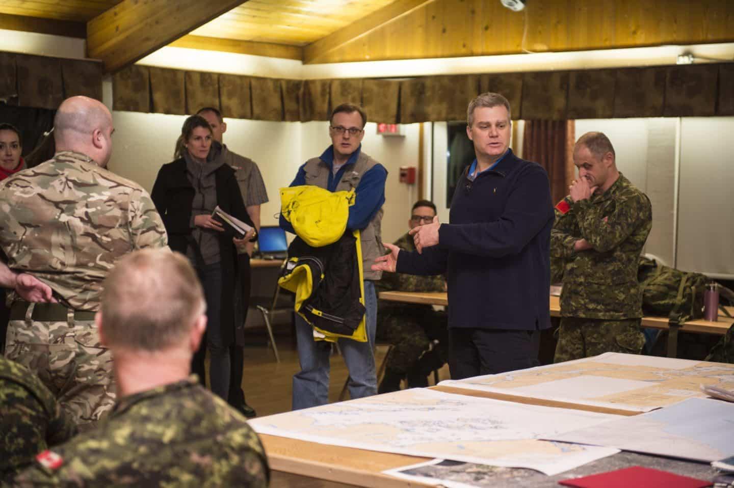 Military personnel in discussion around a table with maps, indoors.
