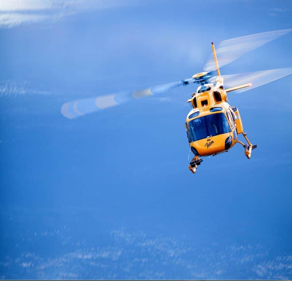 Yellow helicopter flying against a clear blue sky.