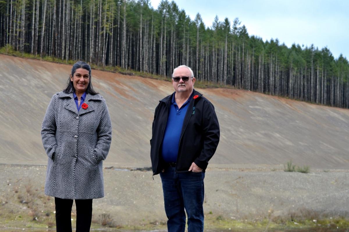 Two people stand outside in front of a forest, wearing coats with red poppies.