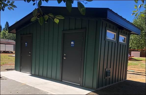 Green public restroom building with two doors under a clear blue sky.