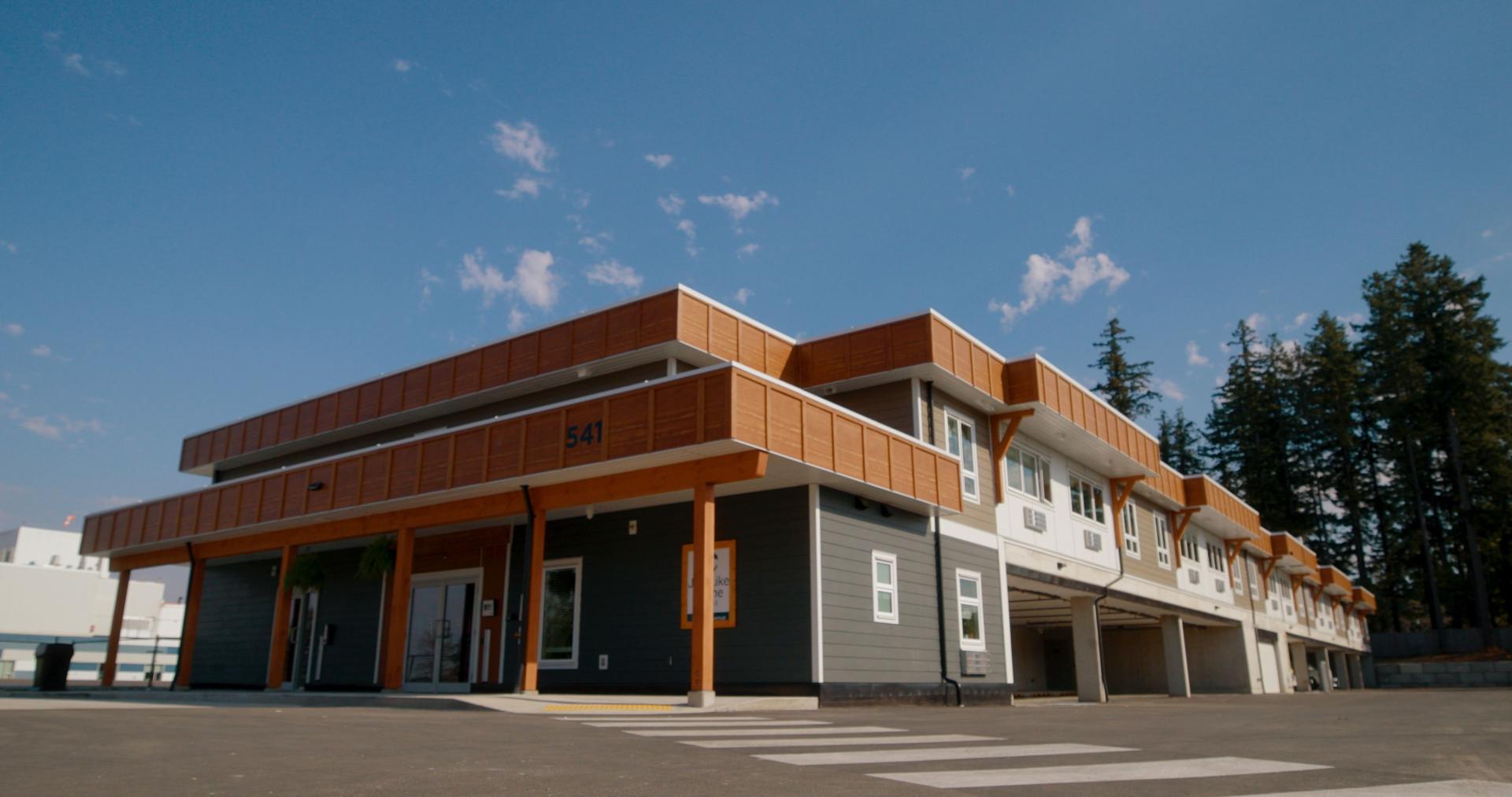 Modern building with wooden accents and large windows, set against a blue sky.